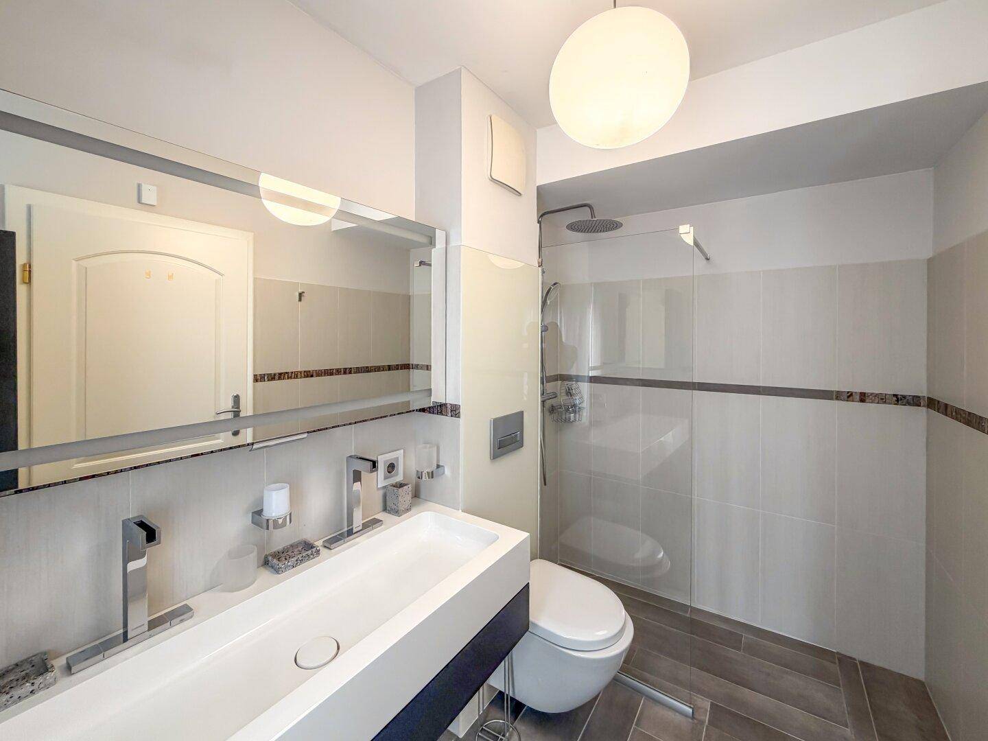 Modernes Badezimmer mit Waschtisch, wandhängendem WC und großer Duschkabine.