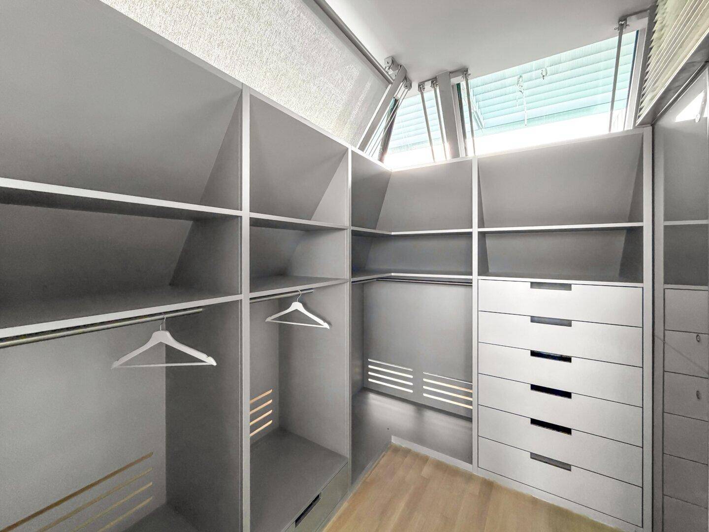 Begehbarer Kleiderschrank mit Einbauschränken, Schubladen und Dachfenstern für Tageslicht.