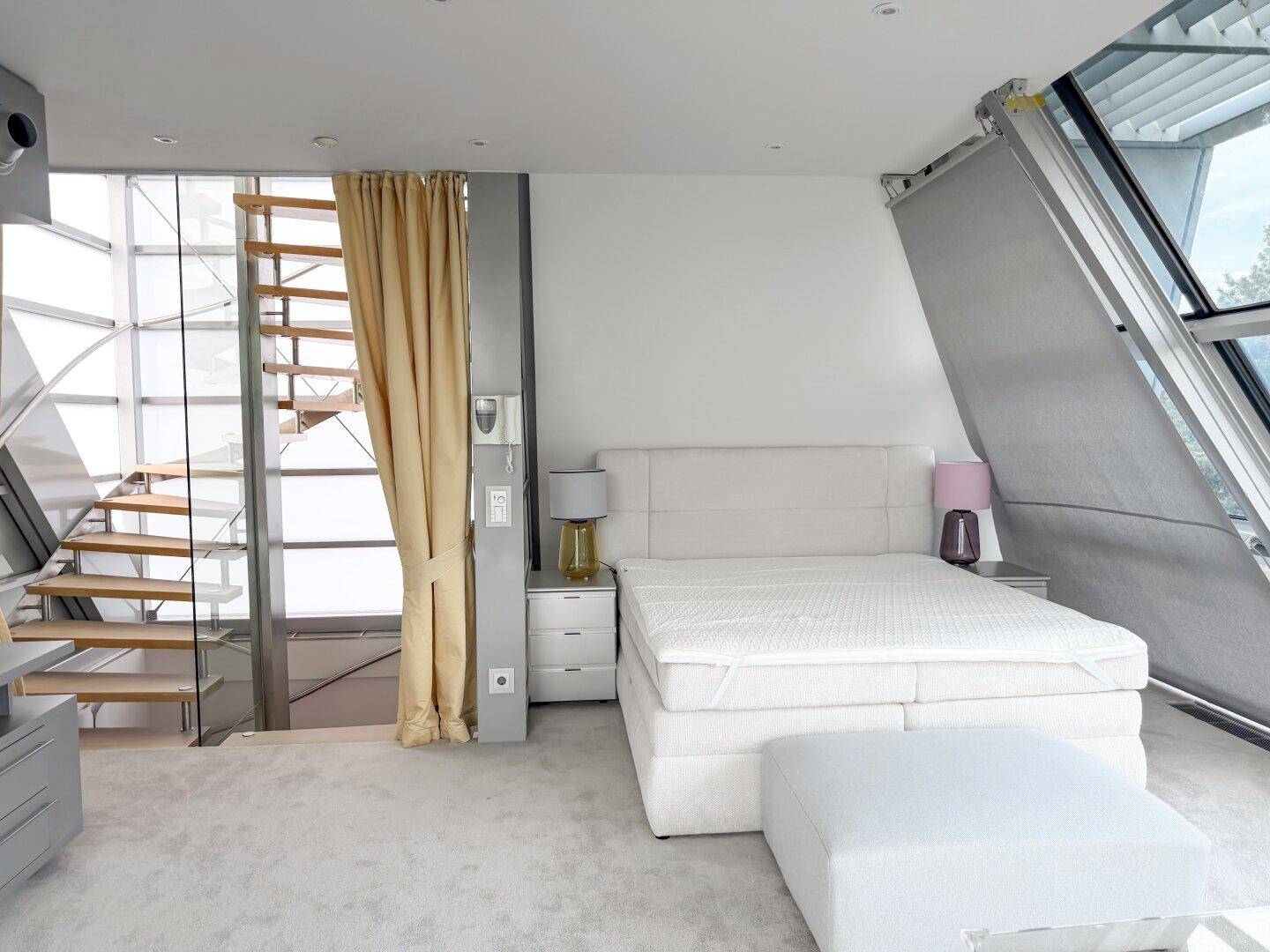 Helles Schlafzimmer im Dachgeschoss mit Glasfassade, Wendeltreppe und Panoramablick.