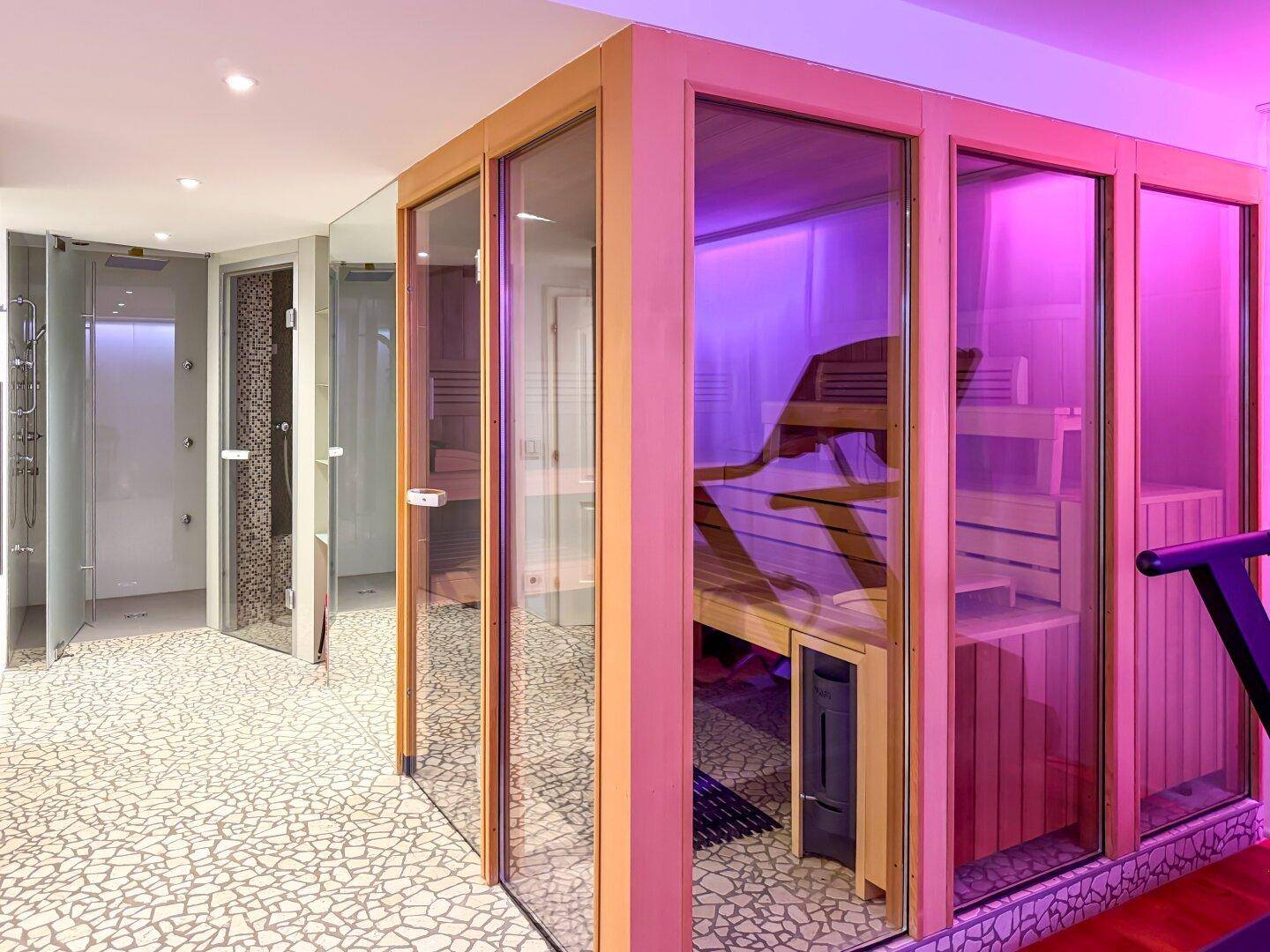Moderner Wellnessbereich mit Sauna, Duschen und farbiger Beleuchtung.