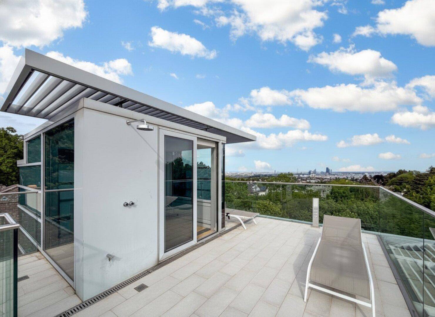 Große Dachterrasse mit Liegestühlen, Außendusche und weitem Blick über die Stadt.