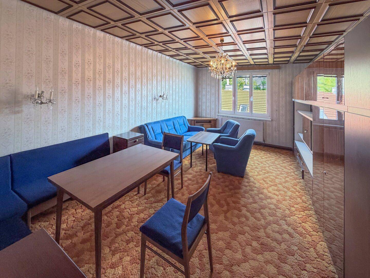 Geräumiges Wohnzimmer mit blauen Sofas, gemusterter Tapete und einer Kassettendecke im traditionellen Stil.