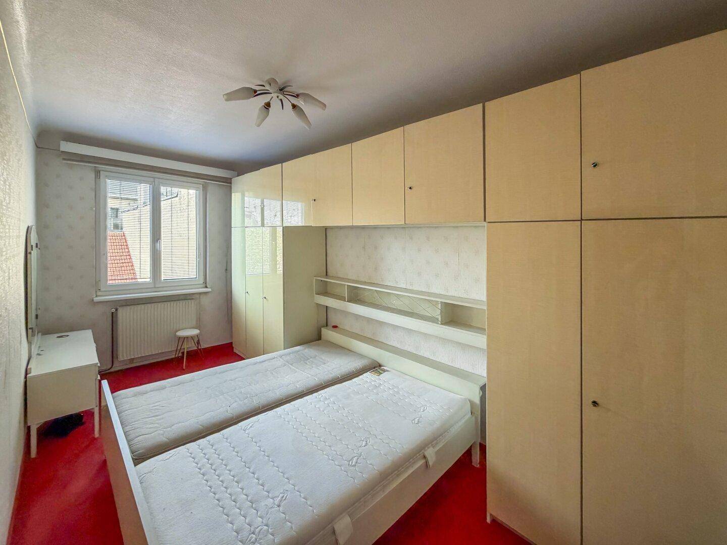 Schlafzimmer mit zwei Einzelbetten, Einbauschränken und einem Fenster, das Tageslicht hereinlässt.