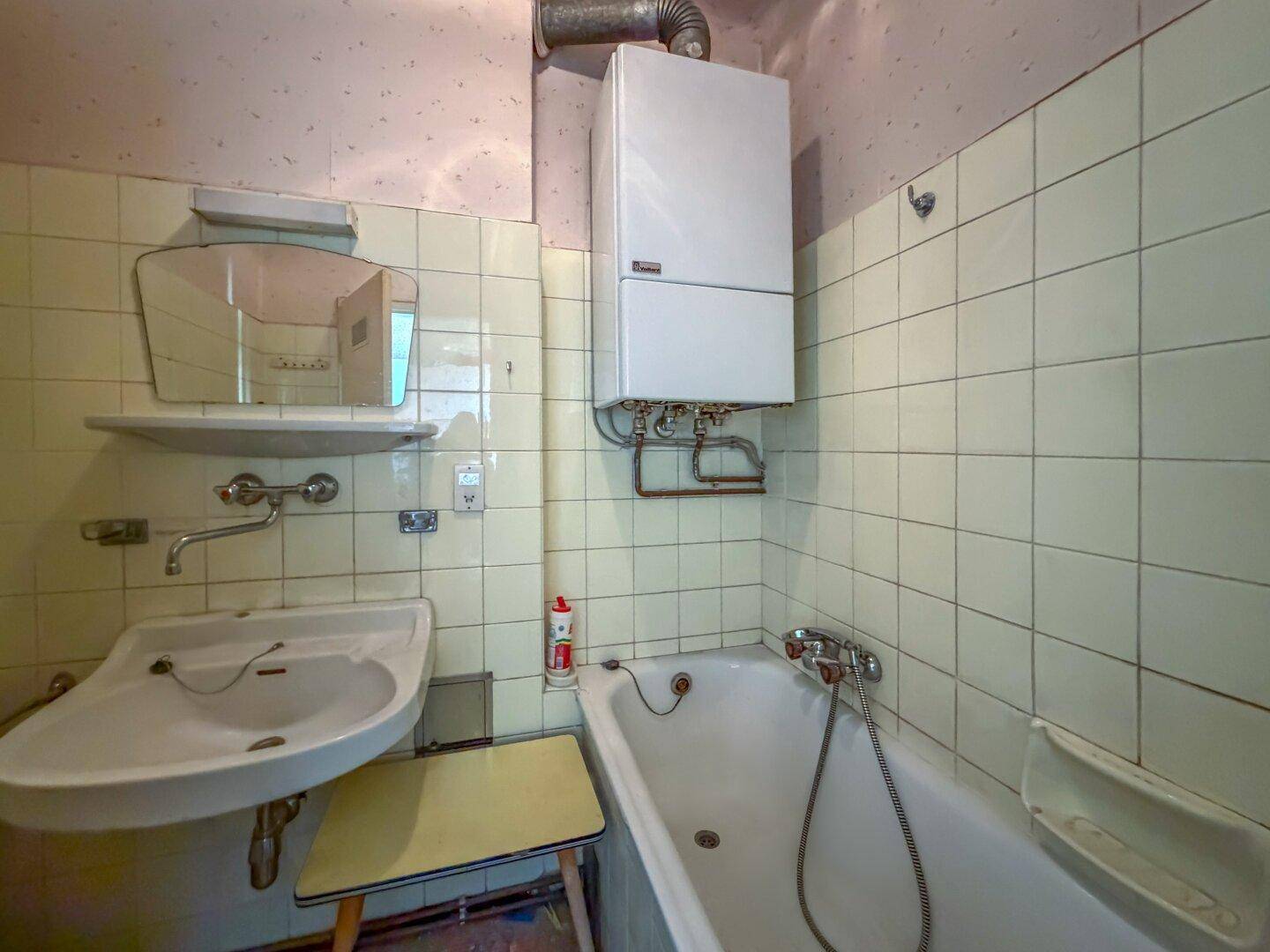Badezimmer mit Badewanne, Waschbecken und einem Wandboiler, ausgestattet mit hellgrünen Fliesen.