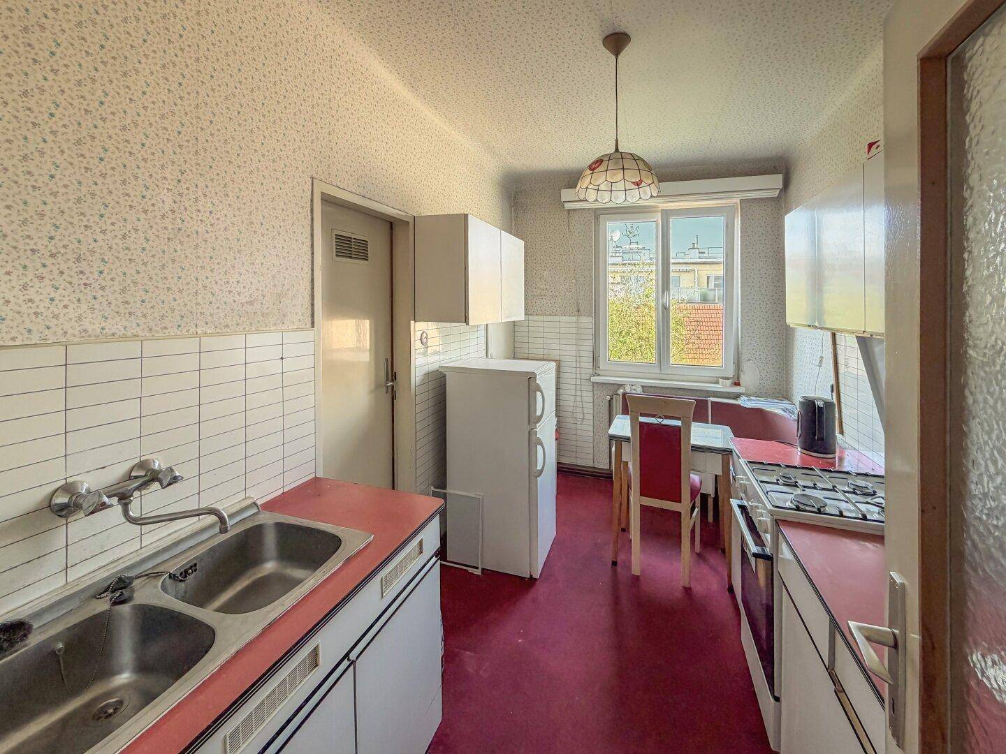 Küche mit roten Arbeitsplatten, Doppelspüle, Gasherd und einem kleinen Essbereich am Fenster.