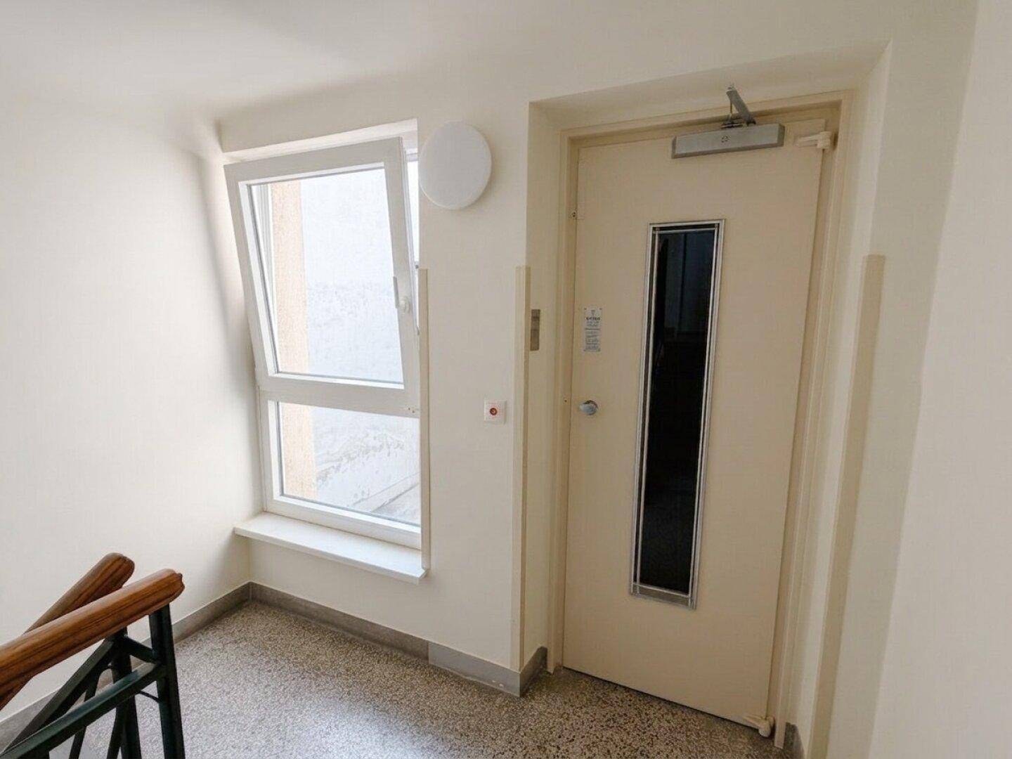 Treppenhausflur mit Fenster und Aufzugstür, gut beleuchtet durch Tageslicht.