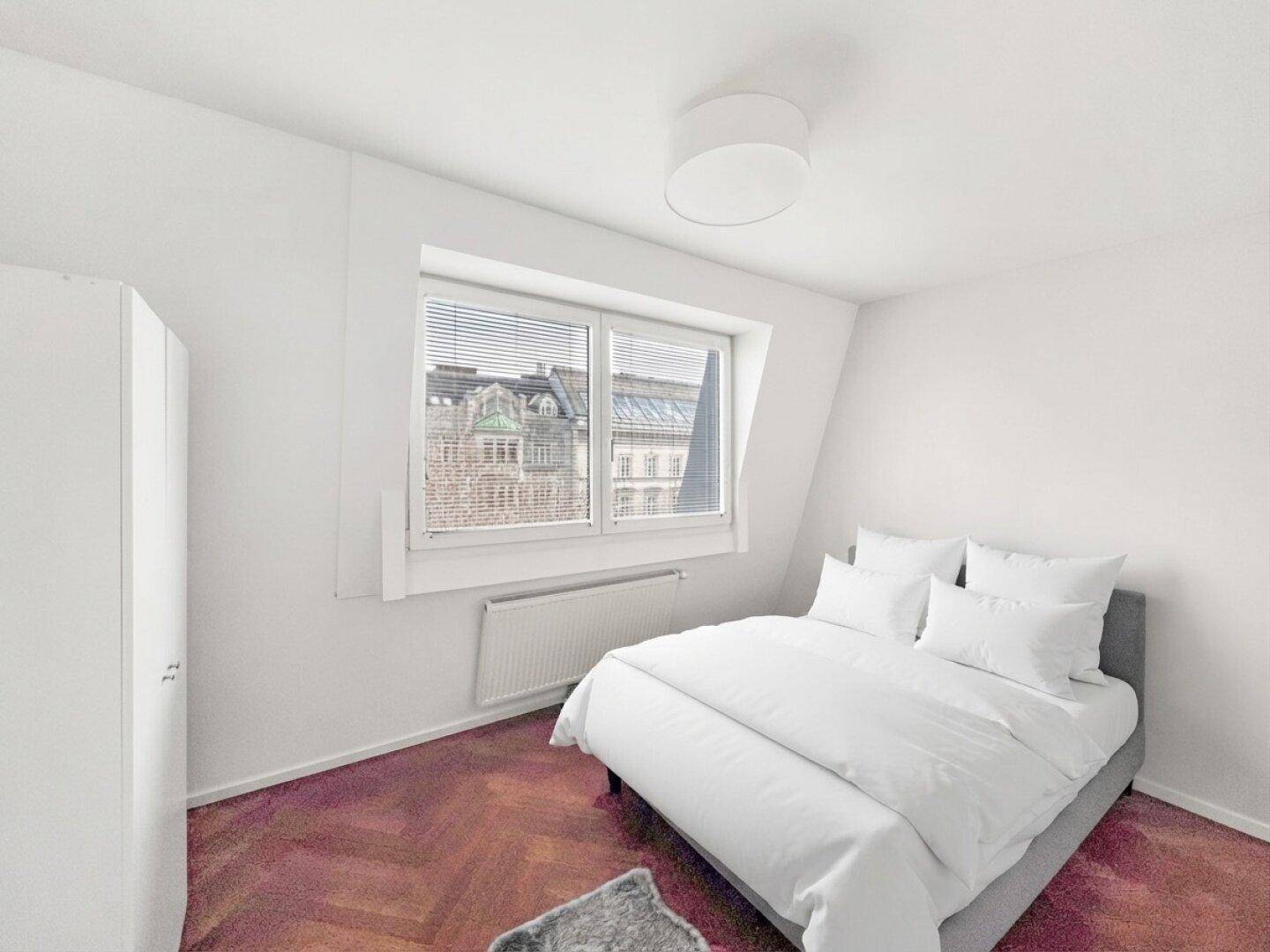 Helles Schlafzimmer mit Doppelbett, Parkettboden und Fenster mit Stadtblick.