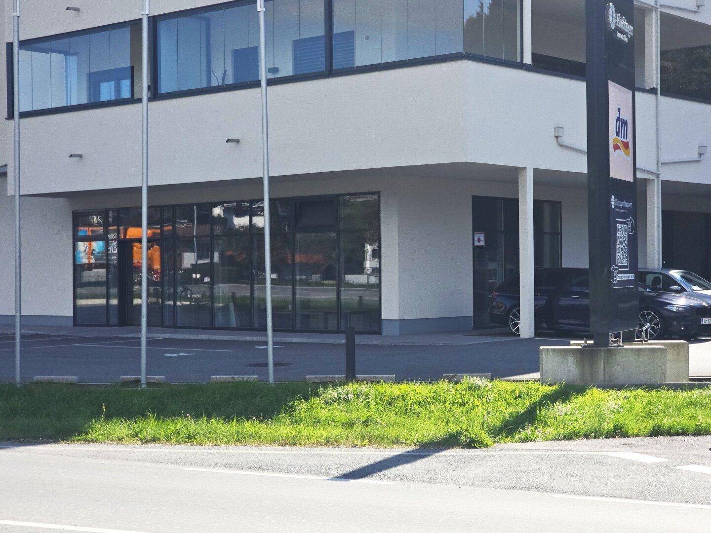 Detailansicht des Erdgeschosses mit Eingangsbereich, Schaufenstern und einem Teil des Parkplatzes mit dm-Schild.