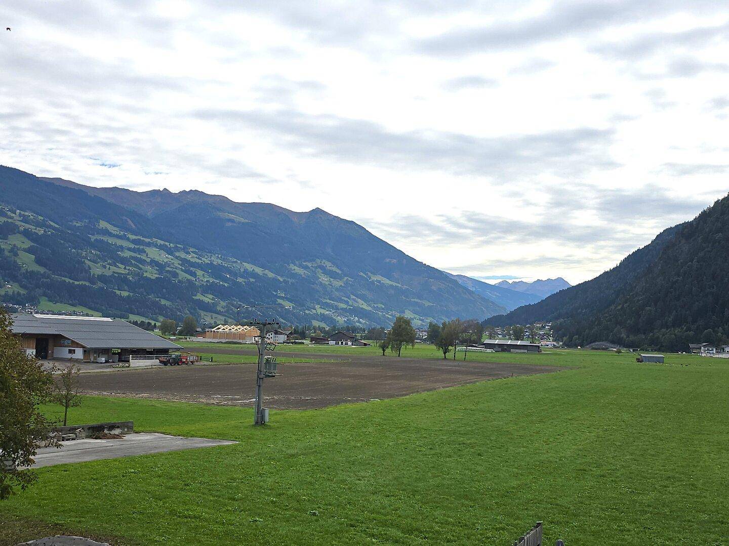 Weitläufige Landschaft mit grünen Wiesen und majestätischen Bergen unter bewölktem Himmel.