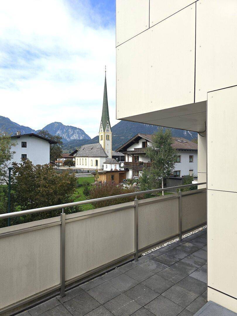 Balkon mit Fliesenboden und malerischem Blick auf ein Dorf mit Kirche und Berge.