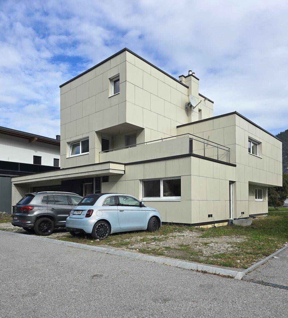 Modernes Wohnhaus mit heller Fassade, klaren Linien und geparkten Fahrzeugen davor.
