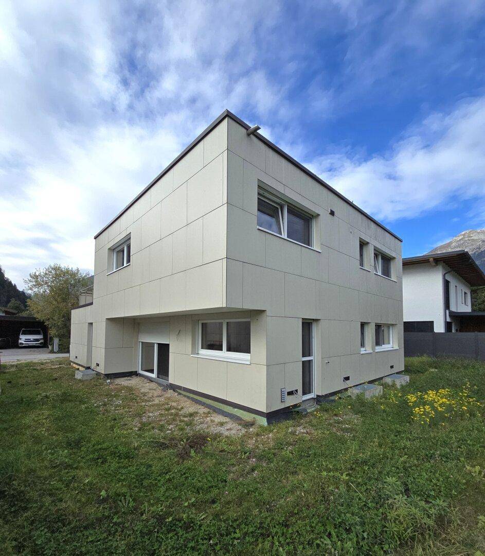 Modernes Wohnhaus mit heller Fassadenverkleidung und flachem Dach, umgeben von Grünflächen.