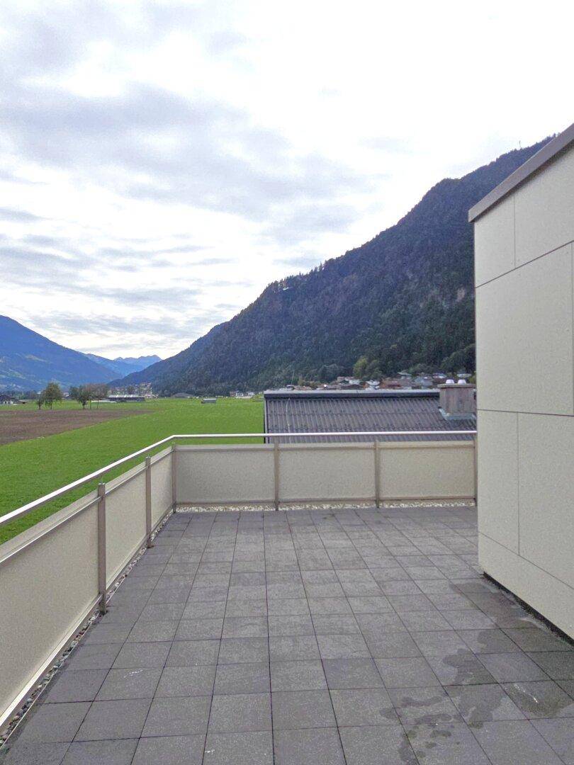 Große Terrasse mit Fliesenboden und Panoramablick auf grüne Wiesen und Berge.