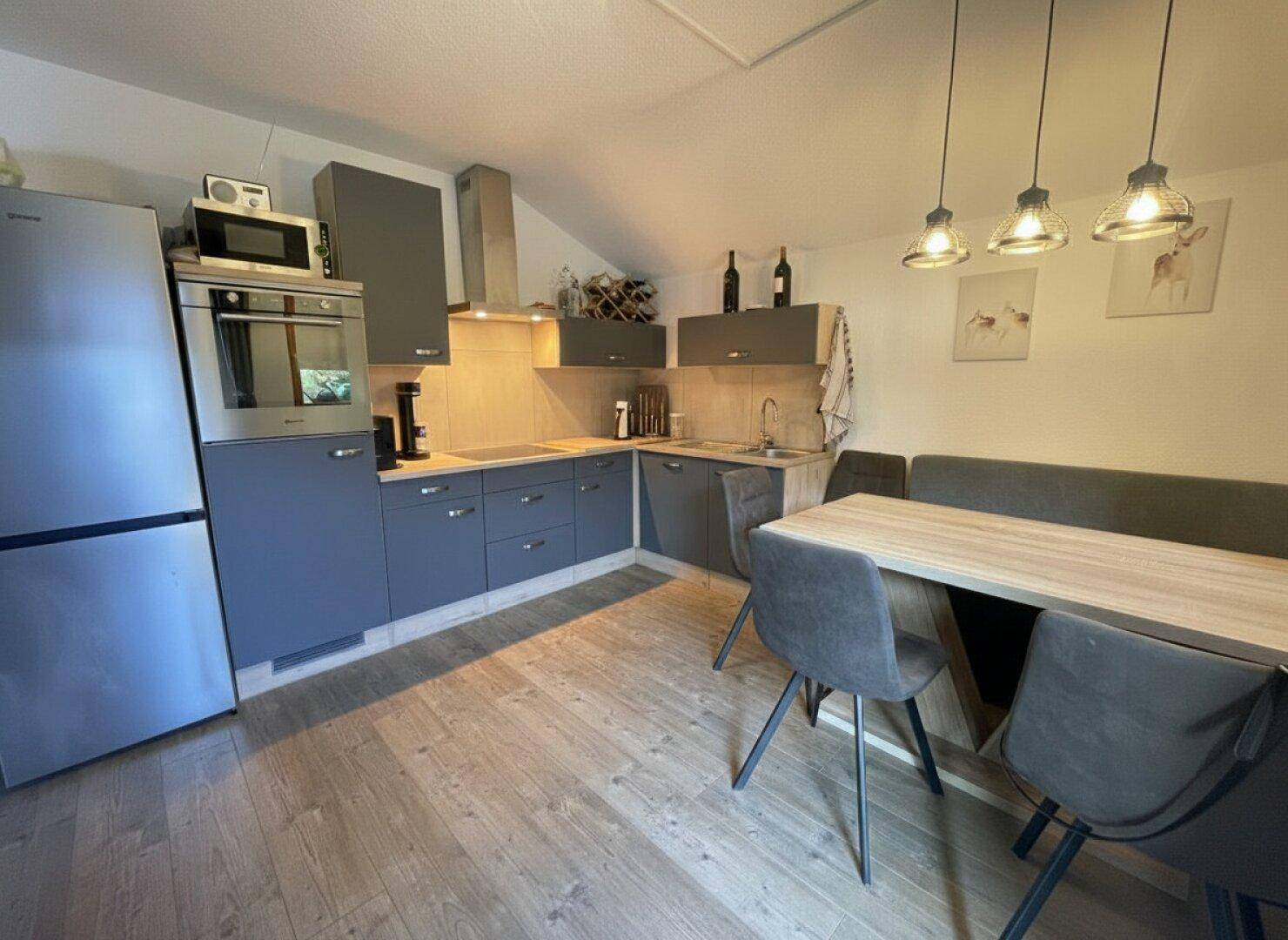 Moderne Einbauküche in Grau mit Essbereich, ausgestattet mit Kühlschrank und Backofen.