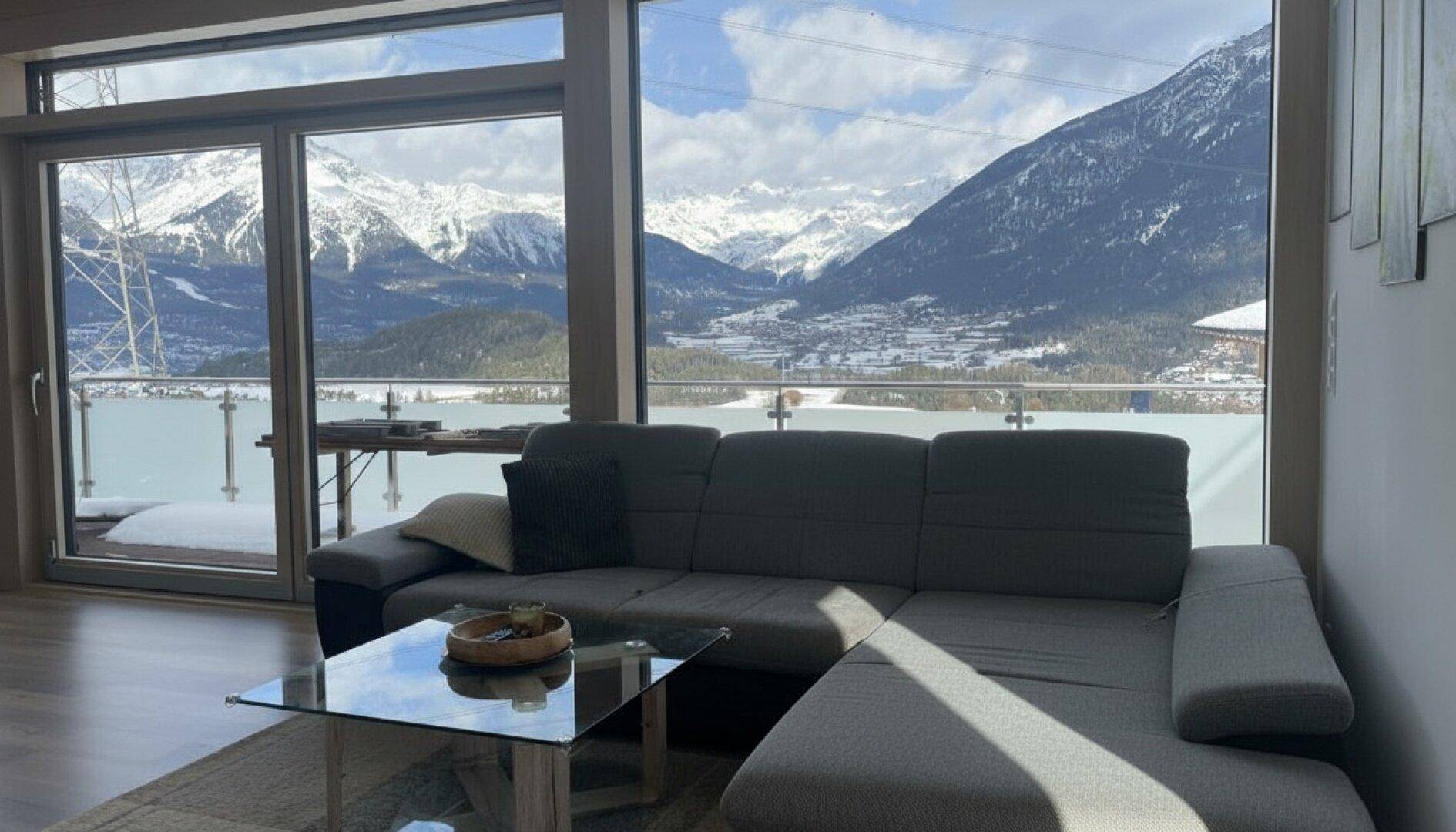Gemütlicher Wohnbereich mit Ecksofa und Panoramafenstern mit Blick auf die verschneiten Berge.