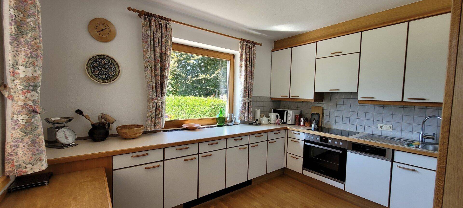 Helle Küche mit weißen Schränken, Holztheke und einem Fenster mit Blick ins Grüne.