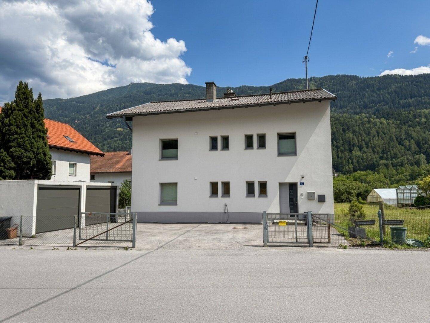 Vorderansicht des Wohnhauses mit Zufahrt und Bergblick unter blauem Himmel.