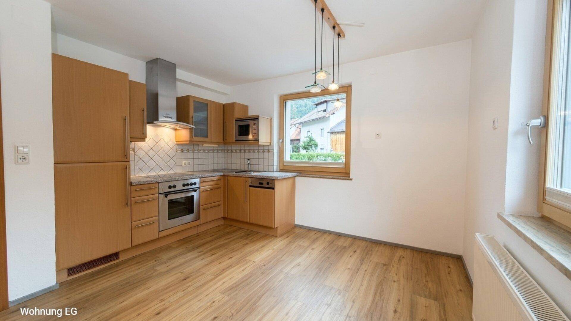 Helle Einbauküche mit Holzfronten, modernen Geräten und Laminatboden.