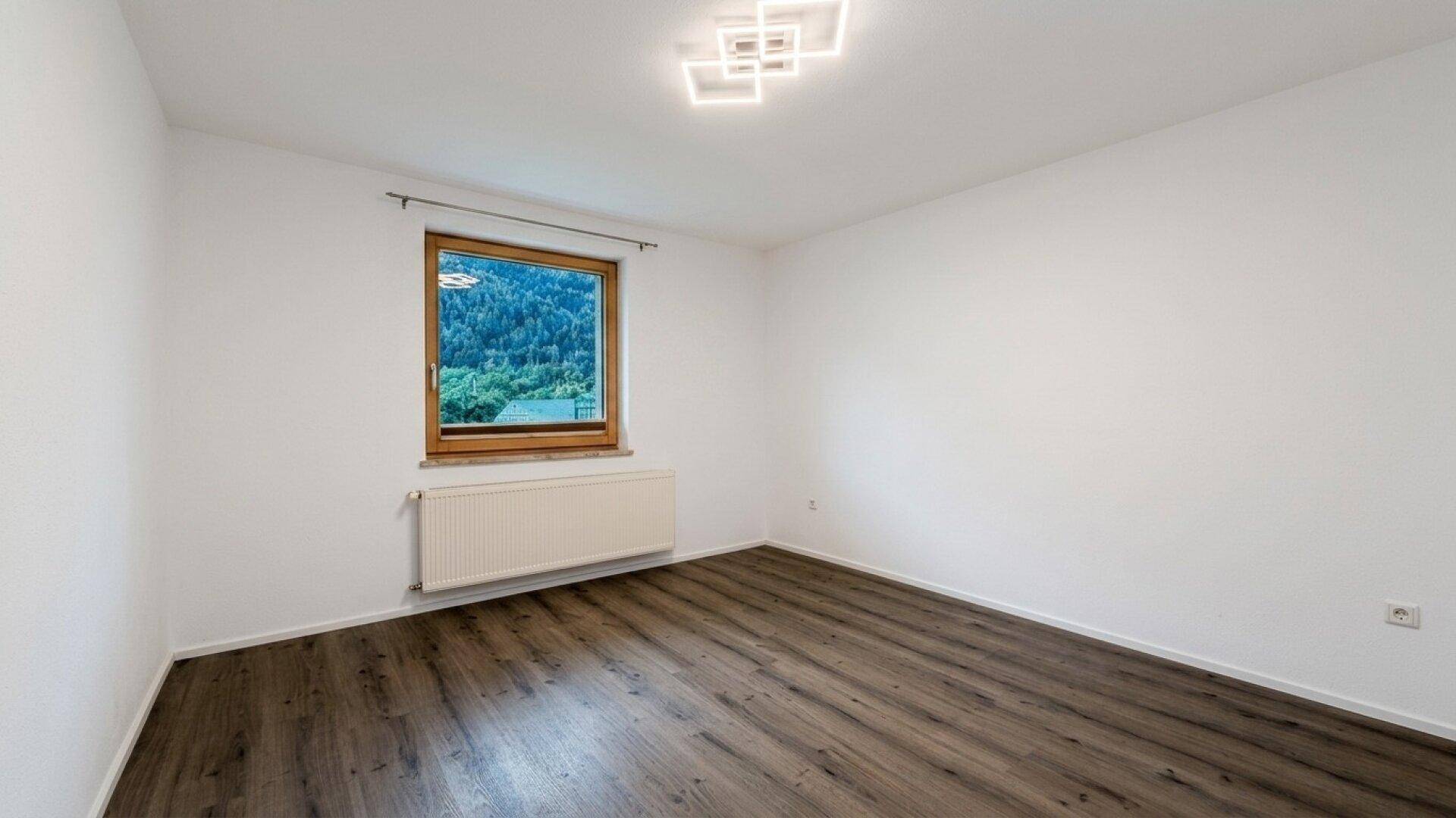 Geräumiges Zimmer mit Laminatboden, weiß gestrichenen Wänden und Bergblick.