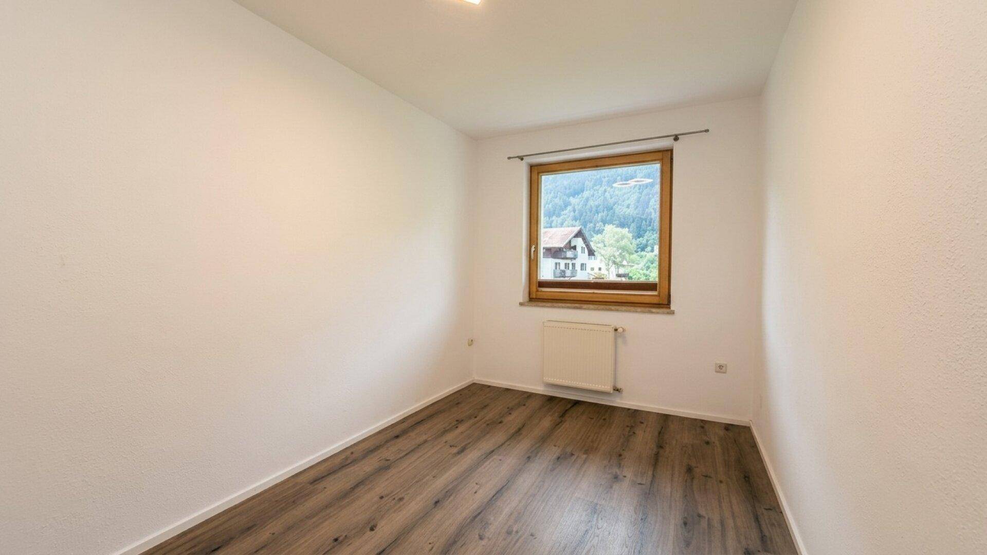 Helles Zimmer mit Laminatboden und Fenster mit Blick auf die Umgebung.