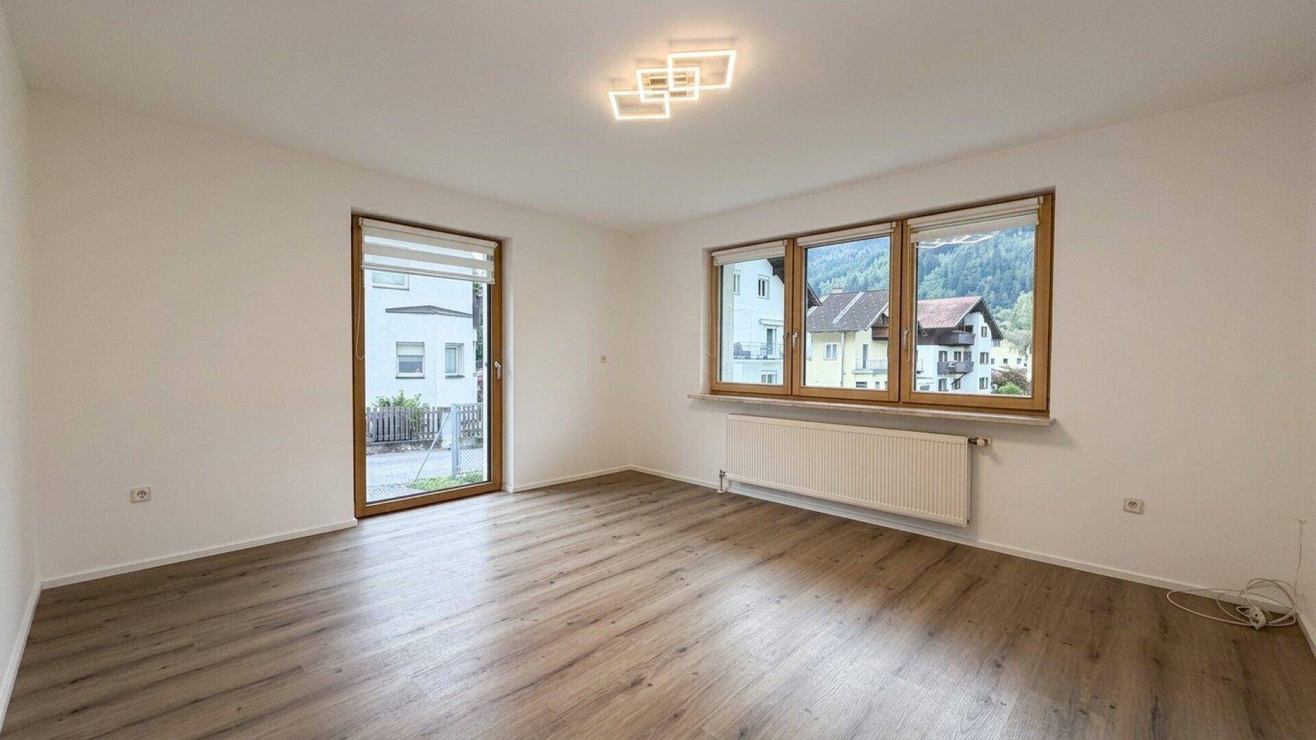 Wohnzimmer mit Laminatboden, großen Fenstern und Zugang zum Außenbereich.