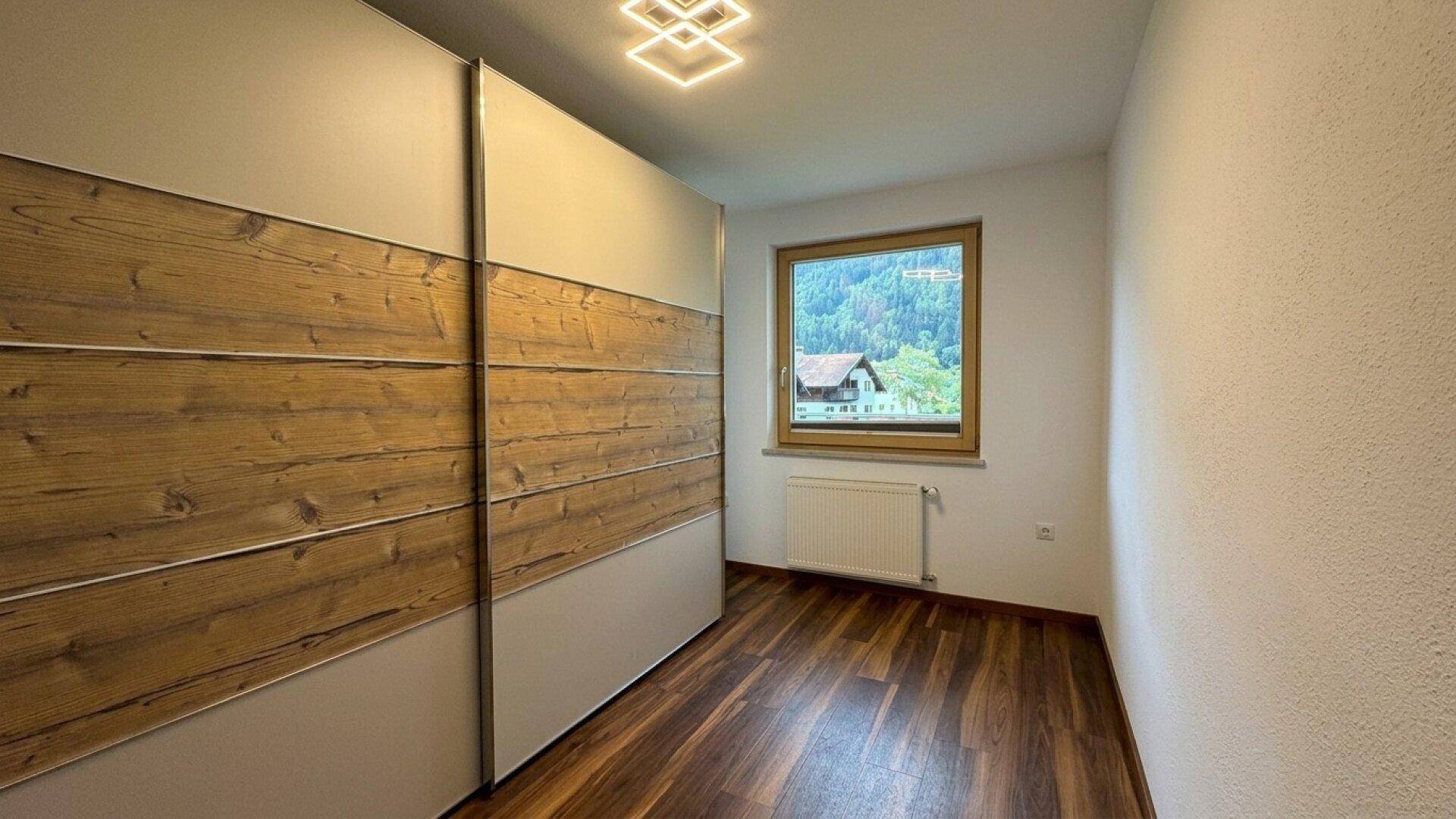 Schlafzimmer mit Laminatboden, Einbauschrank und Fenster mit Bergblick.