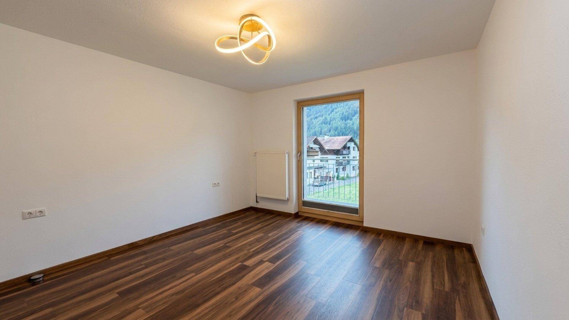 Schlafzimmer mit Laminatboden, moderner Deckenleuchte und Balkonzugang.