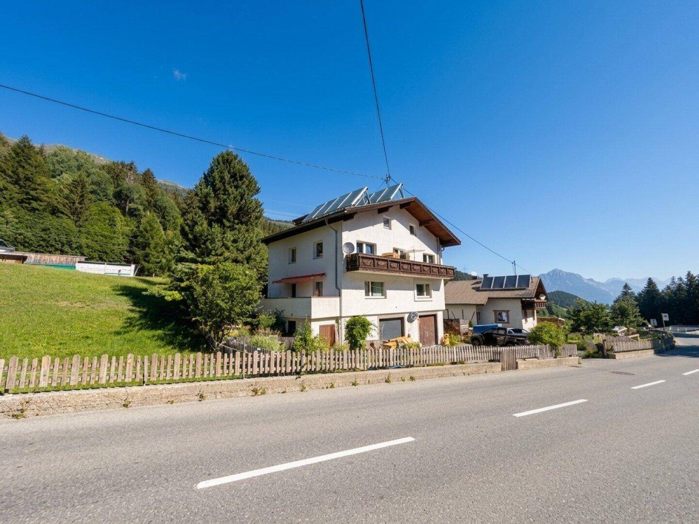Wohnhaus mit Solaranlage, Holzbalkon und Blick auf die umliegende Berglandschaft.