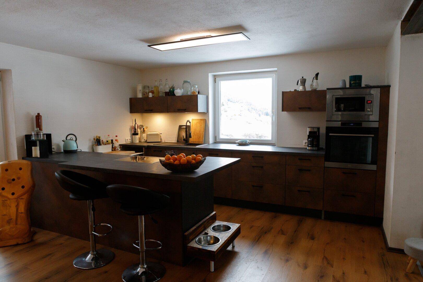 Moderne Küche mit Kücheninsel, dunklen Schränken und Holzboden.