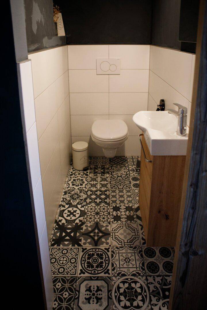 Gäste-WC mit Wand-WC, kleinem Waschbecken und auffälligen gemusterten Bodenfliesen.