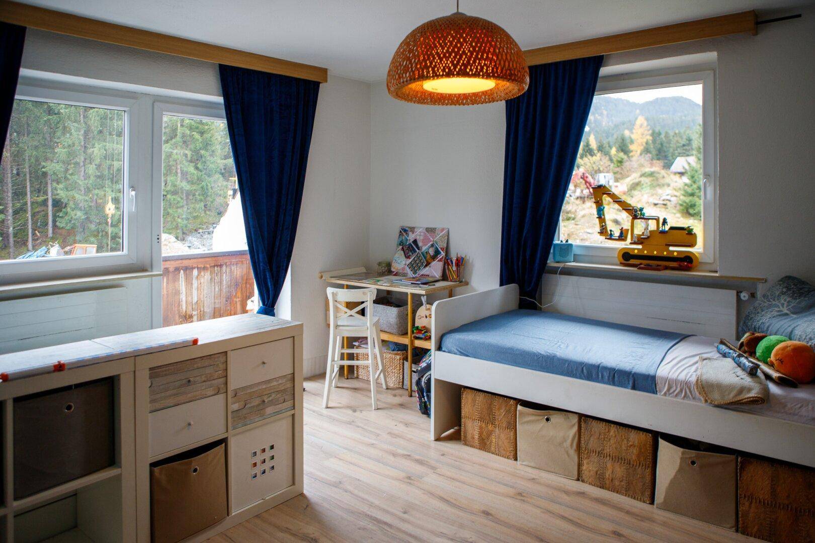 Kinderzimmer mit Einzelbett, Schreibtisch und großen Fenstern mit Blick ins Grüne.