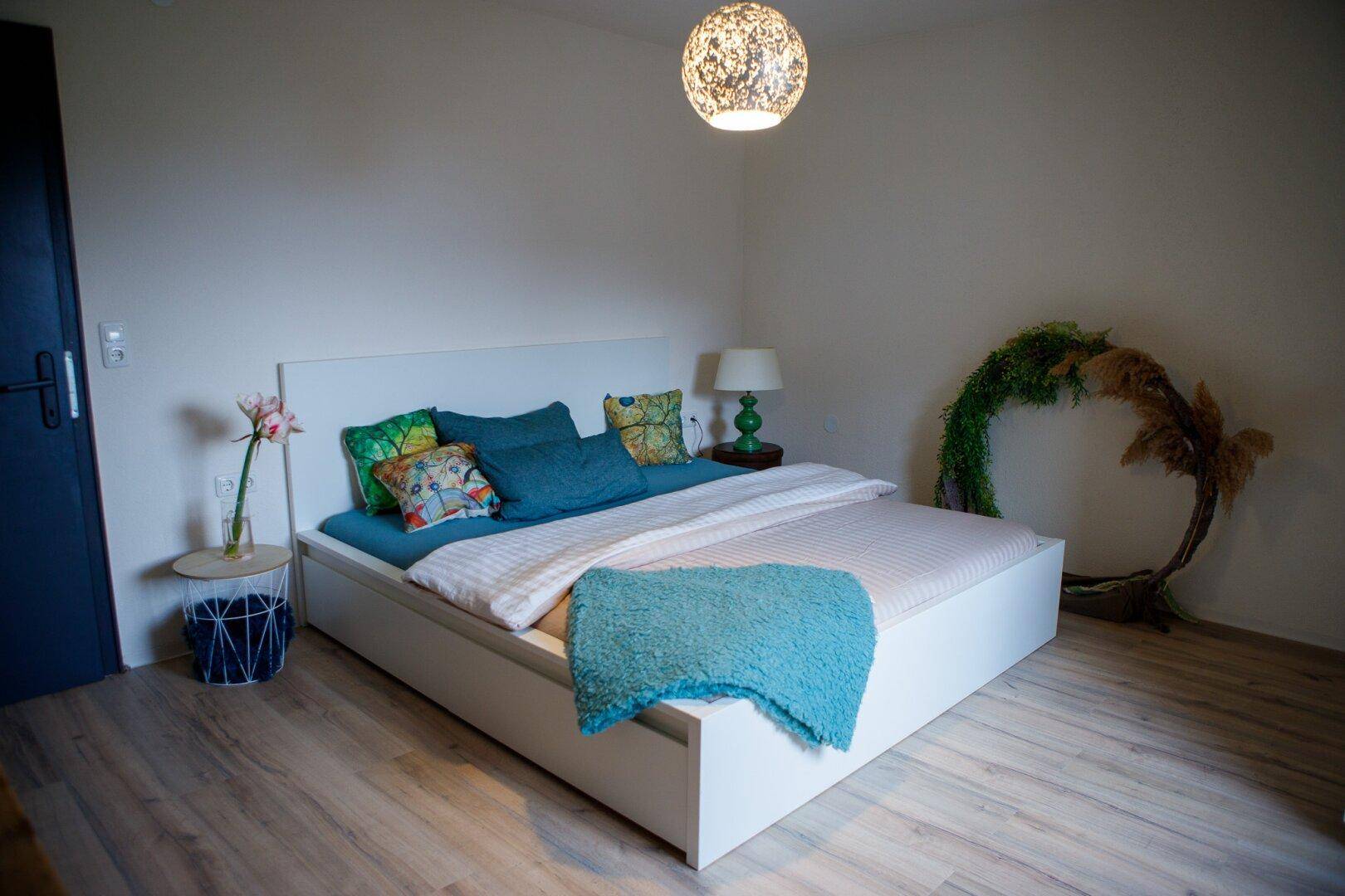 Helles Schlafzimmer mit Doppelbett, Nachttisch und dekorativen Elementen.