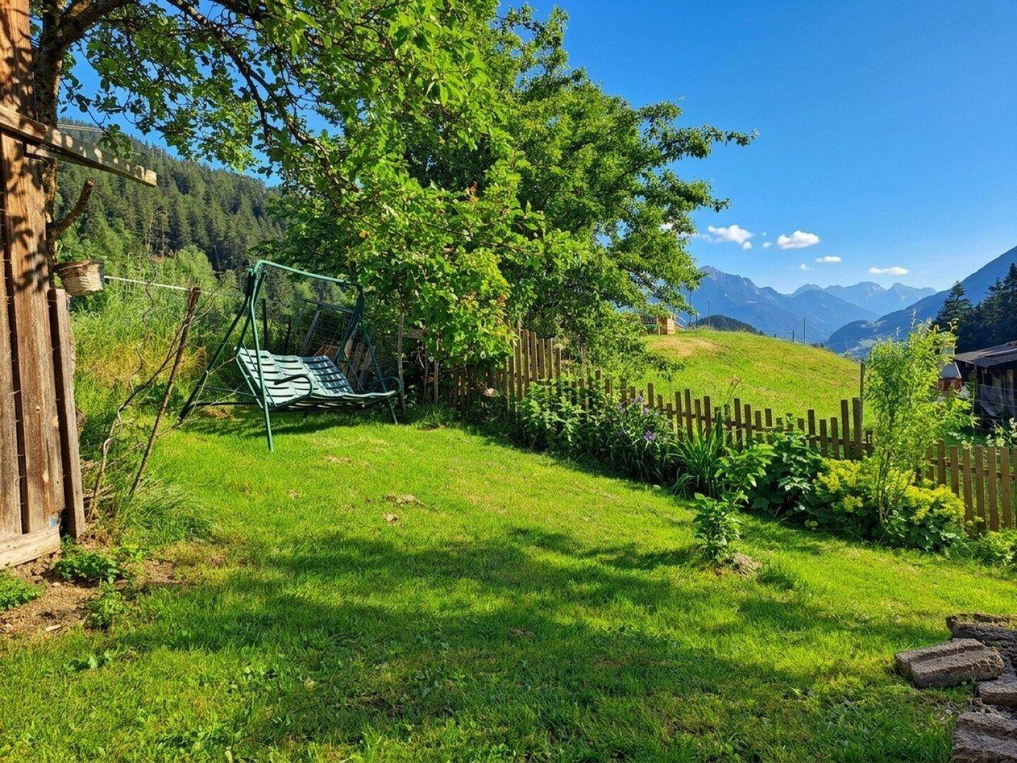 Grüner Gartenbereich mit Schaukel, Holzzaun und weitem Blick auf die Berge.