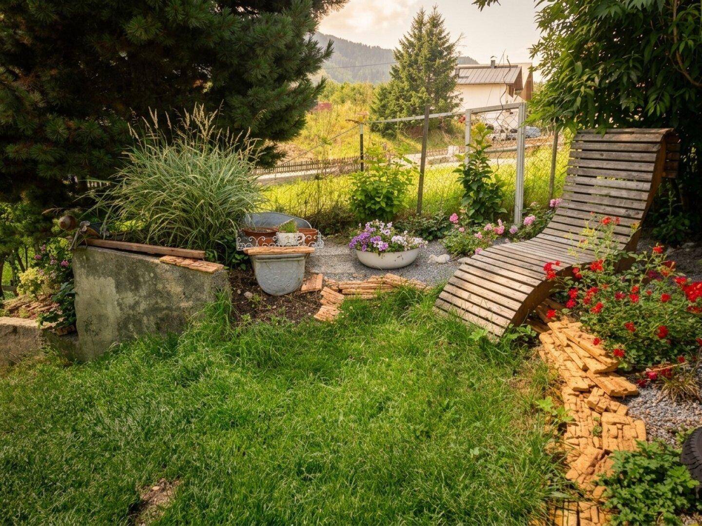 Entspannungsbereich im Garten mit Holzliege, Blumenbeeten und üppigem Grün.