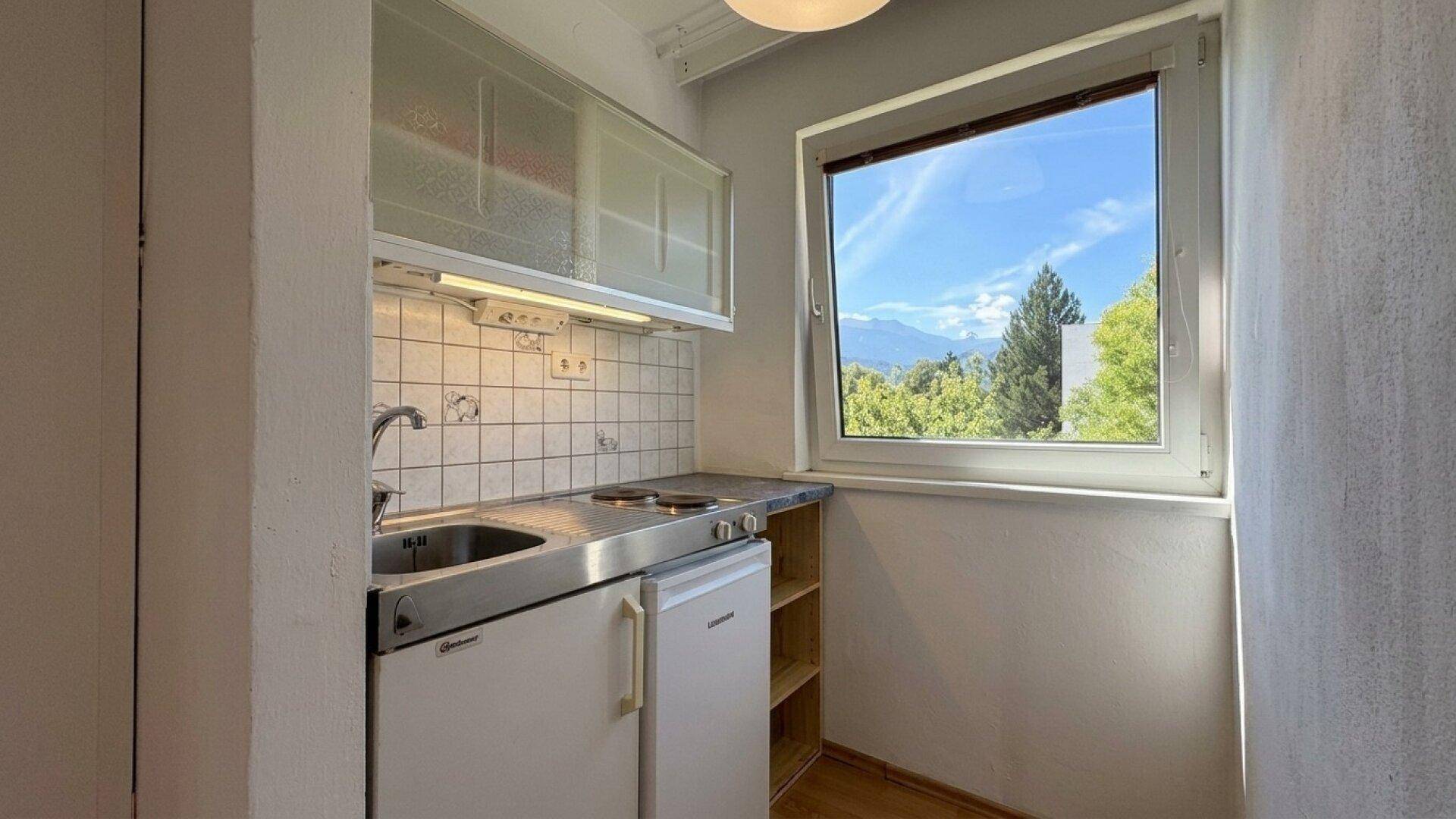 Kleine Kochnische mit Spüle, Kochplatten und Fenster mit Bergblick.