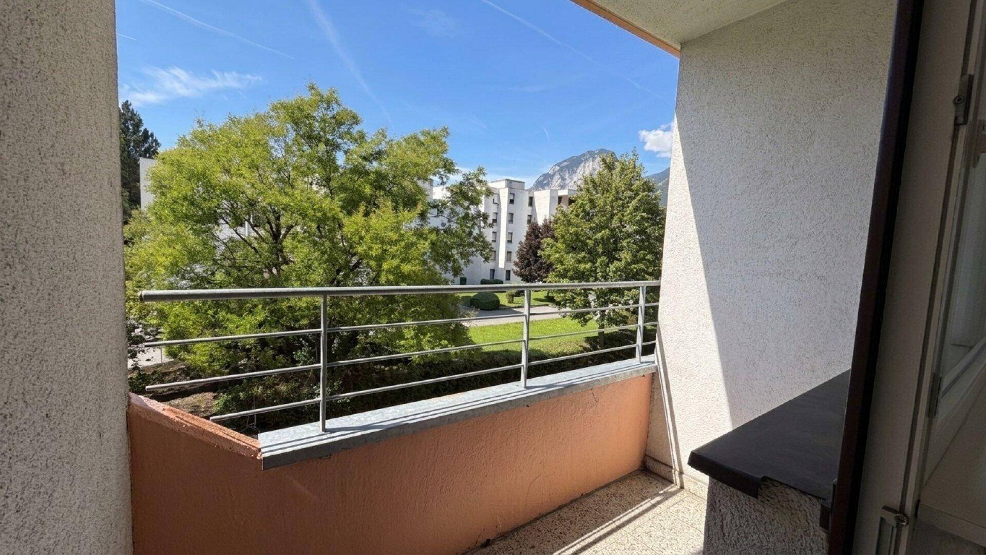 Balkon mit Metallgeländer und Blick auf grüne Bäume und umliegende Gebäude.