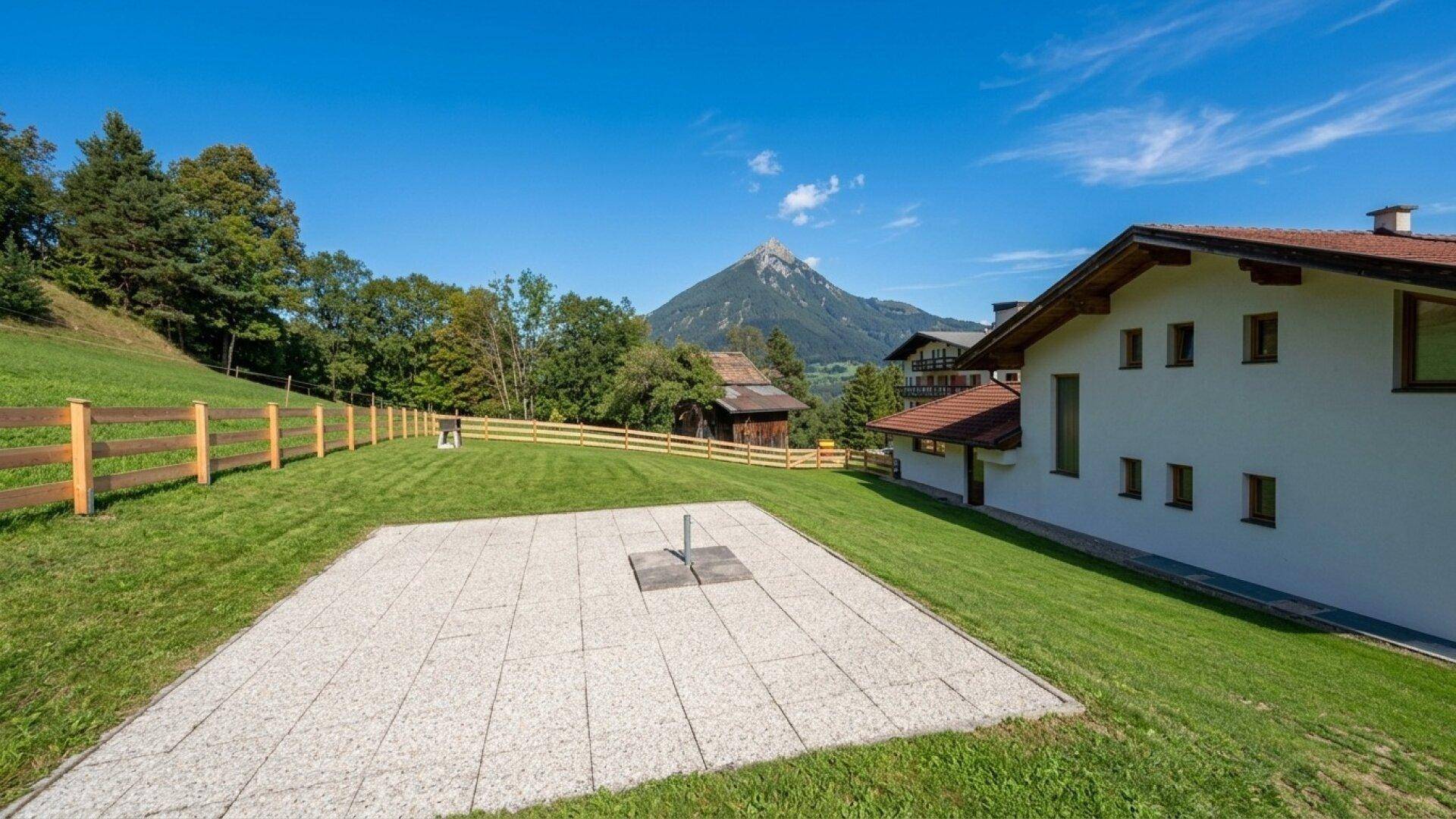 Weitläufige Rasenfläche mit gepflastertem Bereich und Blick auf die umliegende Berglandschaft.