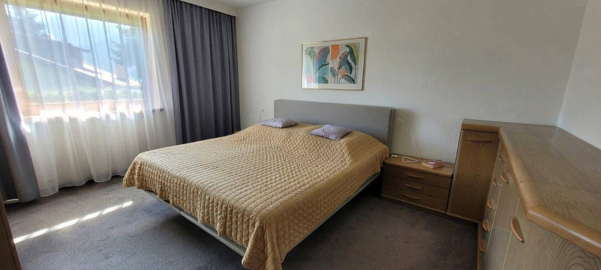 Schlafzimmer mit Doppelbett, Teppichboden und einem großen Fenster mit Vorhängen.
