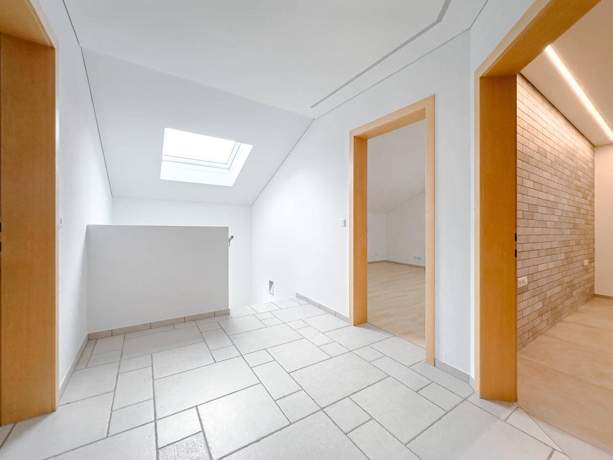 Heller Flur im Dachgeschoss mit Fliesenboden, Dachfenster und Zugang zu weiteren Zimmern.
