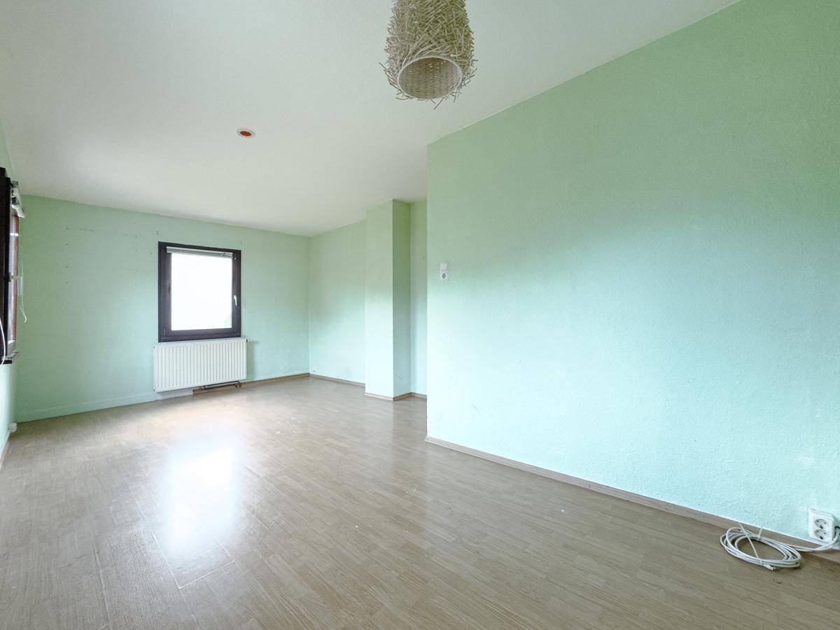 Helles Wohnzimmer mit hellgrünen Wänden und Laminatboden, bietet viel Gestaltungspotenzial.