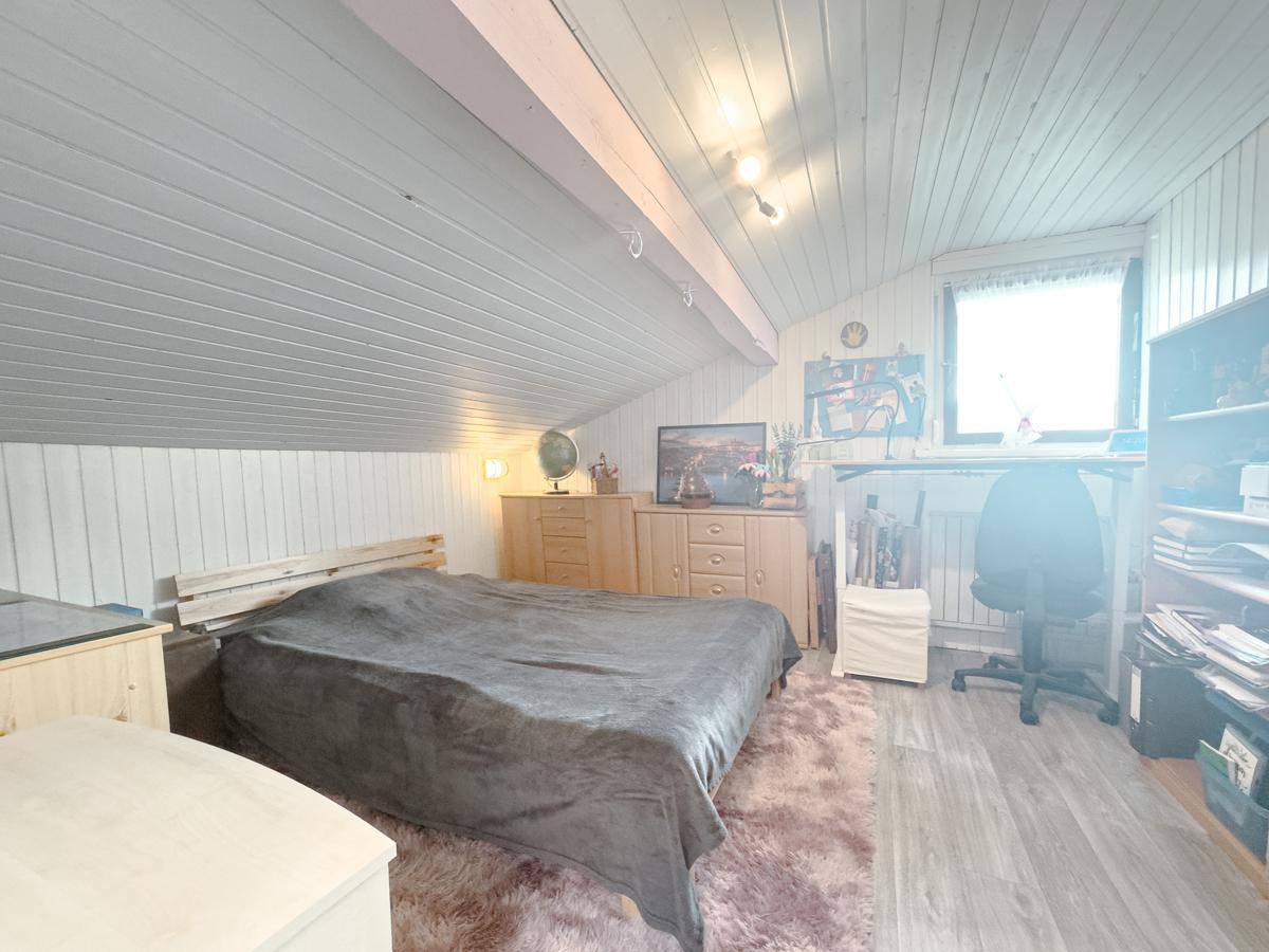 Dachgeschoss-Schlafzimmer mit schrägen Wänden, Holzboden und einem Arbeitsbereich am Fenster.