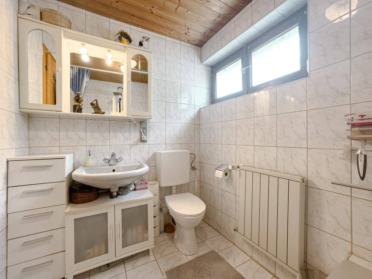 Helles Badezimmer mit WC, Waschbecken, Spiegelschrank und Holzdecke.