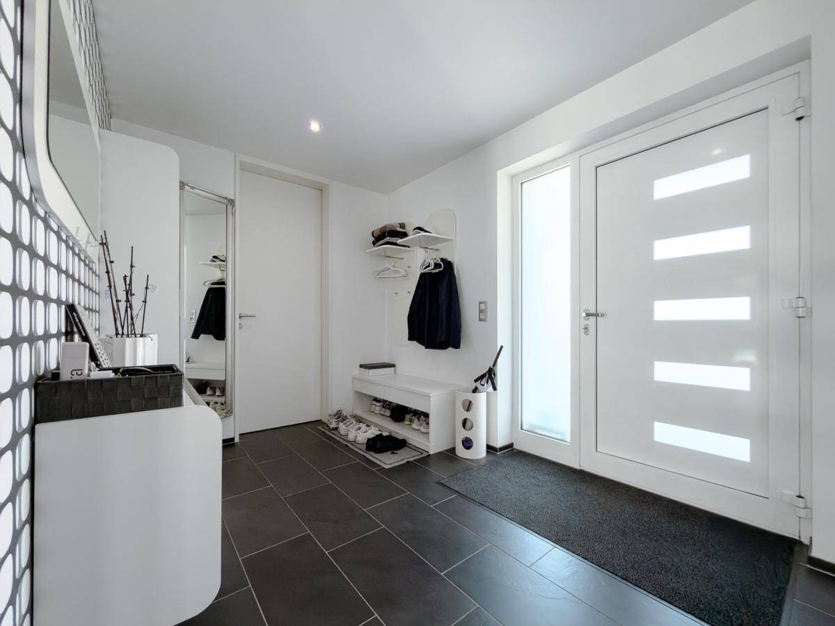 Heller Eingangsbereich mit dunklen Fliesen, Garderobe und modernem Design.