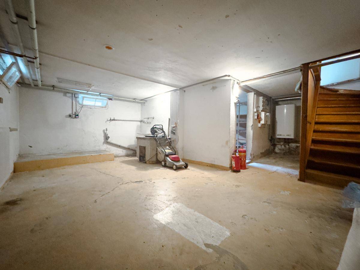 Geräumiger Kellerraum mit Betonboden, sichtbaren Rohren und Holztreppe zum Obergeschoss.