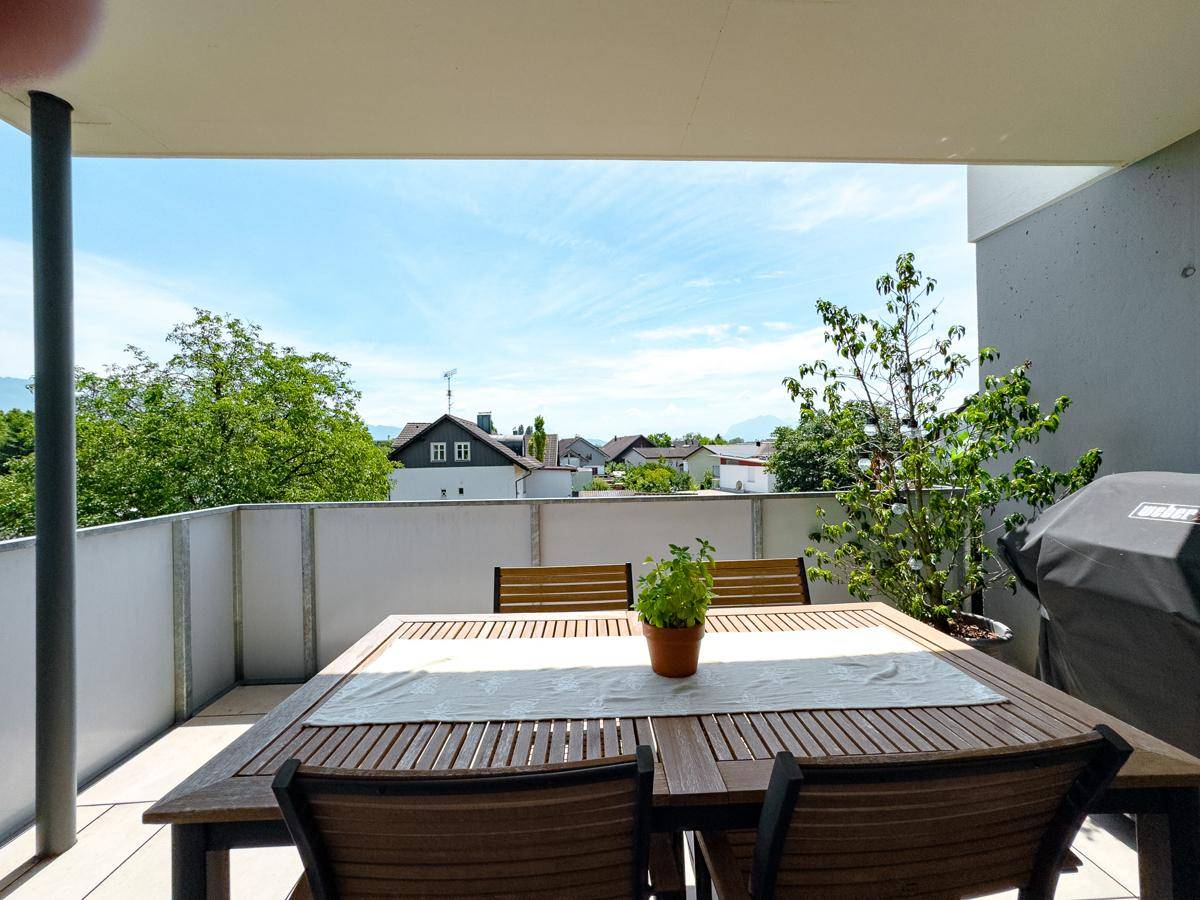 Sonniger Terrassenbereich mit Holztisch und Grill, ideal für Mahlzeiten im Freien.