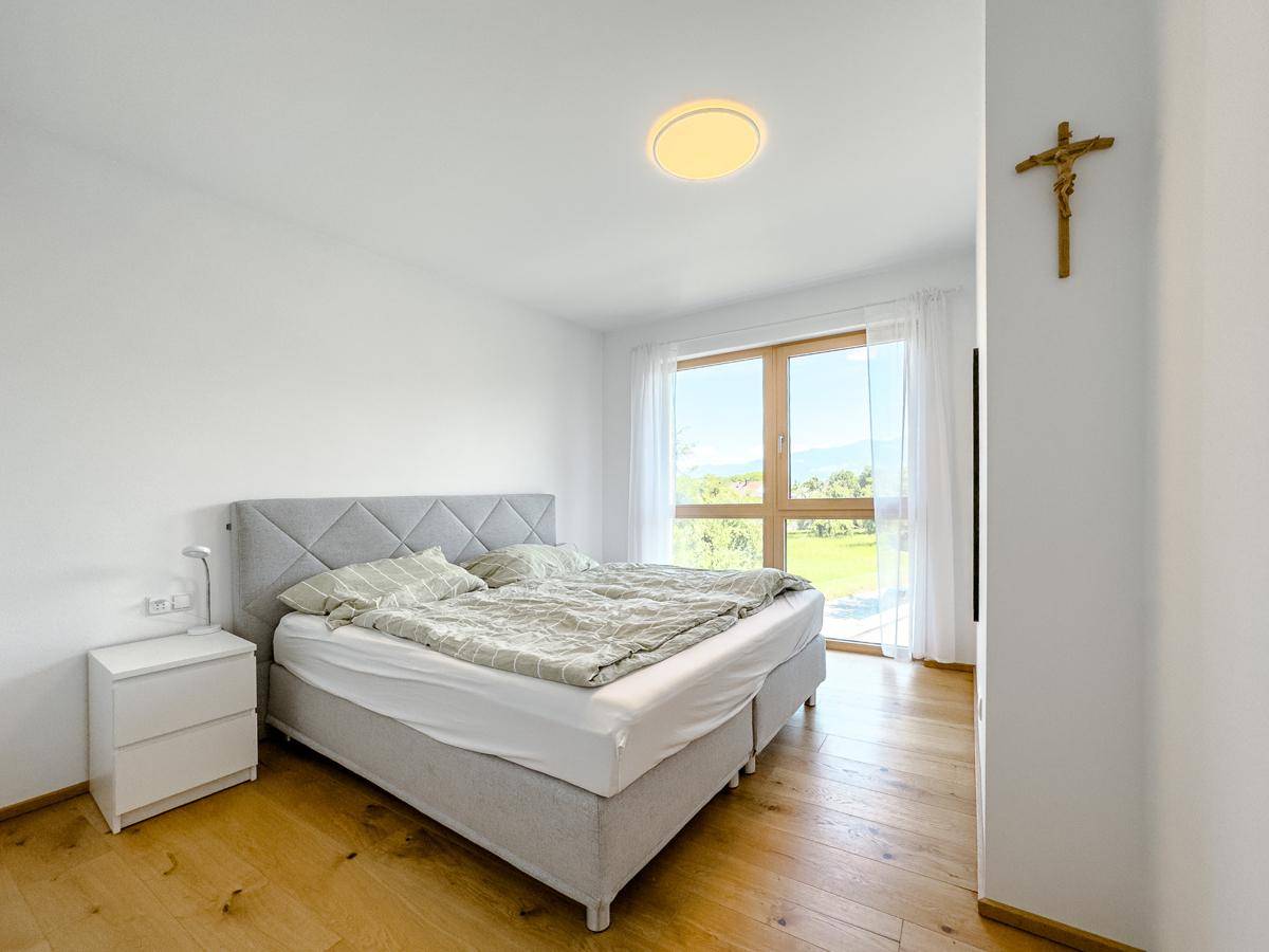 Helles Schlafzimmer mit Holzboden, großem Fenster und Blick ins Grüne.