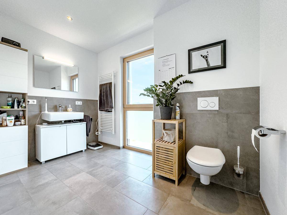 Helles Badezimmer mit WC, Waschtisch, großem Fenster und Fliesenboden.