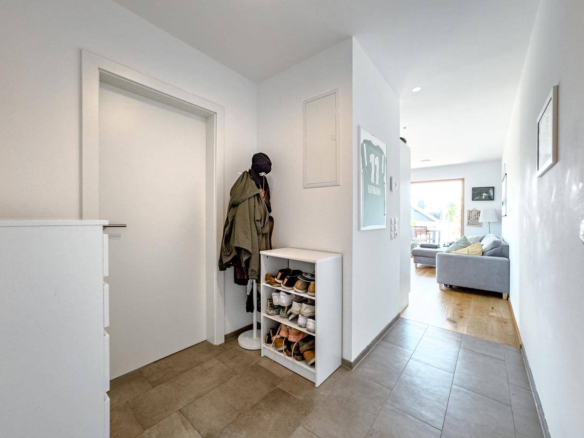 Heller Eingangsbereich mit Fliesenboden, Schuhregal und Garderobe, führt zum Wohnbereich.