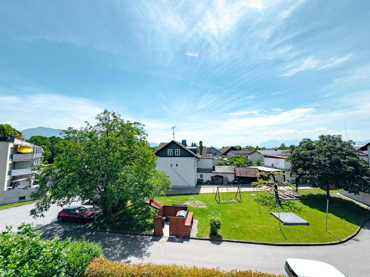 Weitläufiger Blick über die Wohngegend mit Spielplatz, Bäumen und weiteren Gebäuden an einem sonnigen Tag.