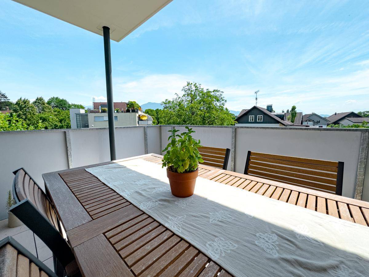 Sonniger Terrassenbereich mit Holztisch und Pflanzen, umgeben von einer niedrigen Mauer.